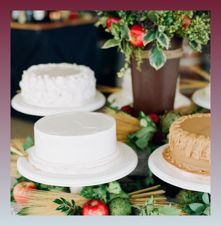 Three cakes on a cake table with potted greenery, apples, and straw