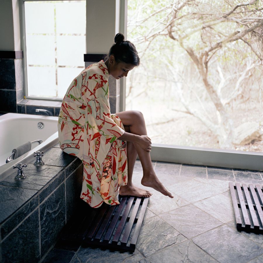 Girl in robe sitting on edge of tub putting lotion on legs