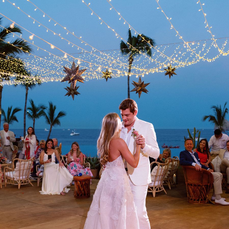 A bride and groom holding hands and dancing beneath string lights and star pendants