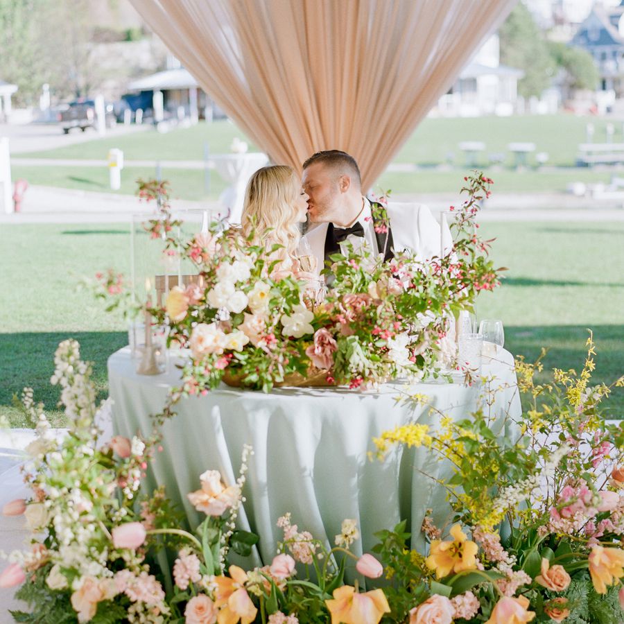 Couple kissing at their sweetheart table covered in blue linens and colorful flowers
