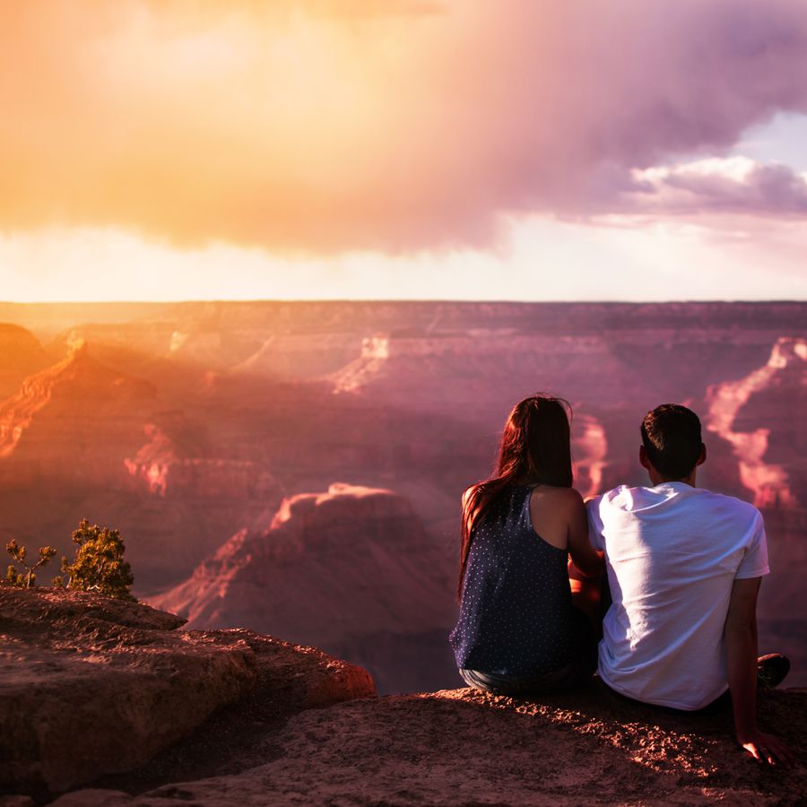 A couple sitting over the Grand Canyon during their Arizona honeymoon.