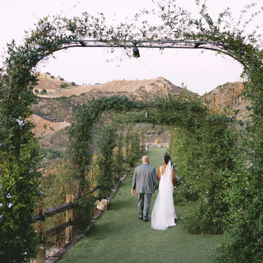 Bride and groom walking hand-in-hand through arches covered in greenery during a destination wedding.