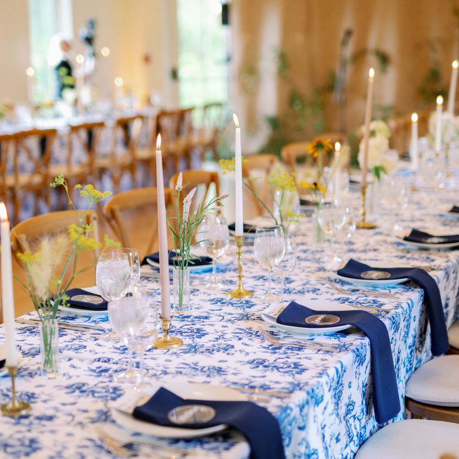 Rehearsal Dinner Venue with Tables Topped with Blue and White Linens, Taper Candles, and Simple Bud Vase Centerpieces