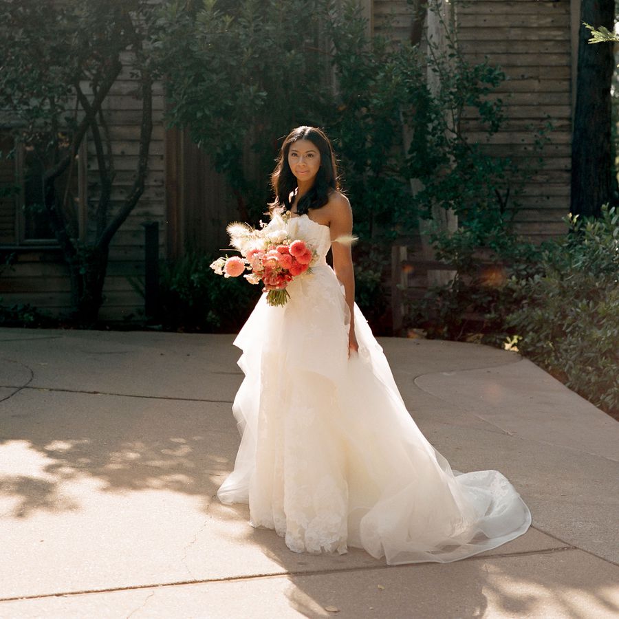 a bride posing with red and pink flowers wearing a strapless wedding dress