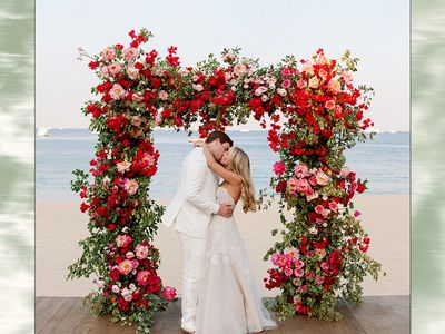 Bride and Groom Kissing Beneath Pink and Red Floral Ceremony Altar at Beachfront Wedding Ceremony