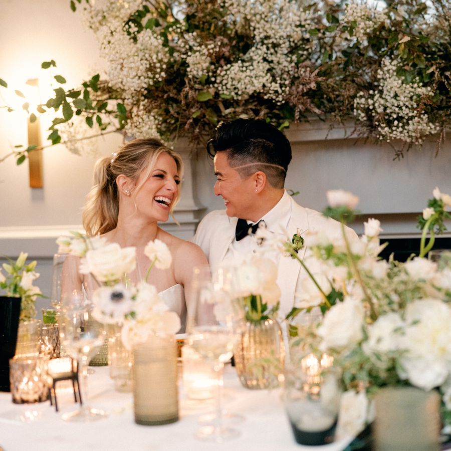 Two Brides in Floral-Filled Wedding Reception Laughing at Funny Wedding Toast