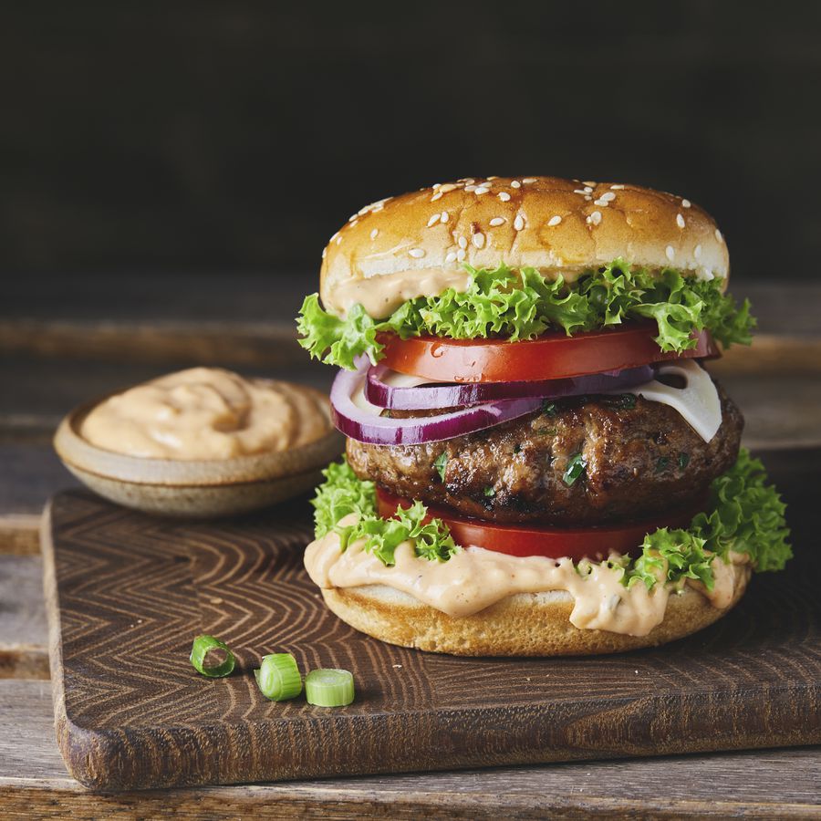 A burger with lettuce, tomato, onions, and sauce on a wooden cutting board
