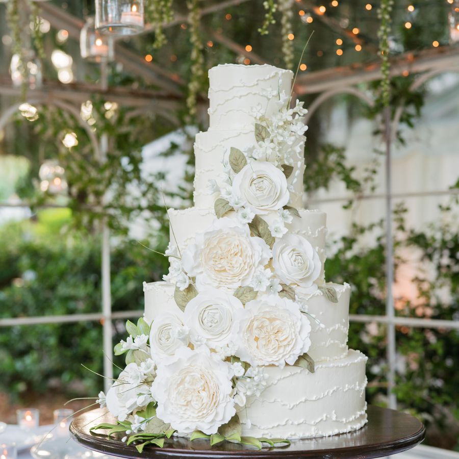 A five-tiered white wedding cake with cascading white flowers and greenery.