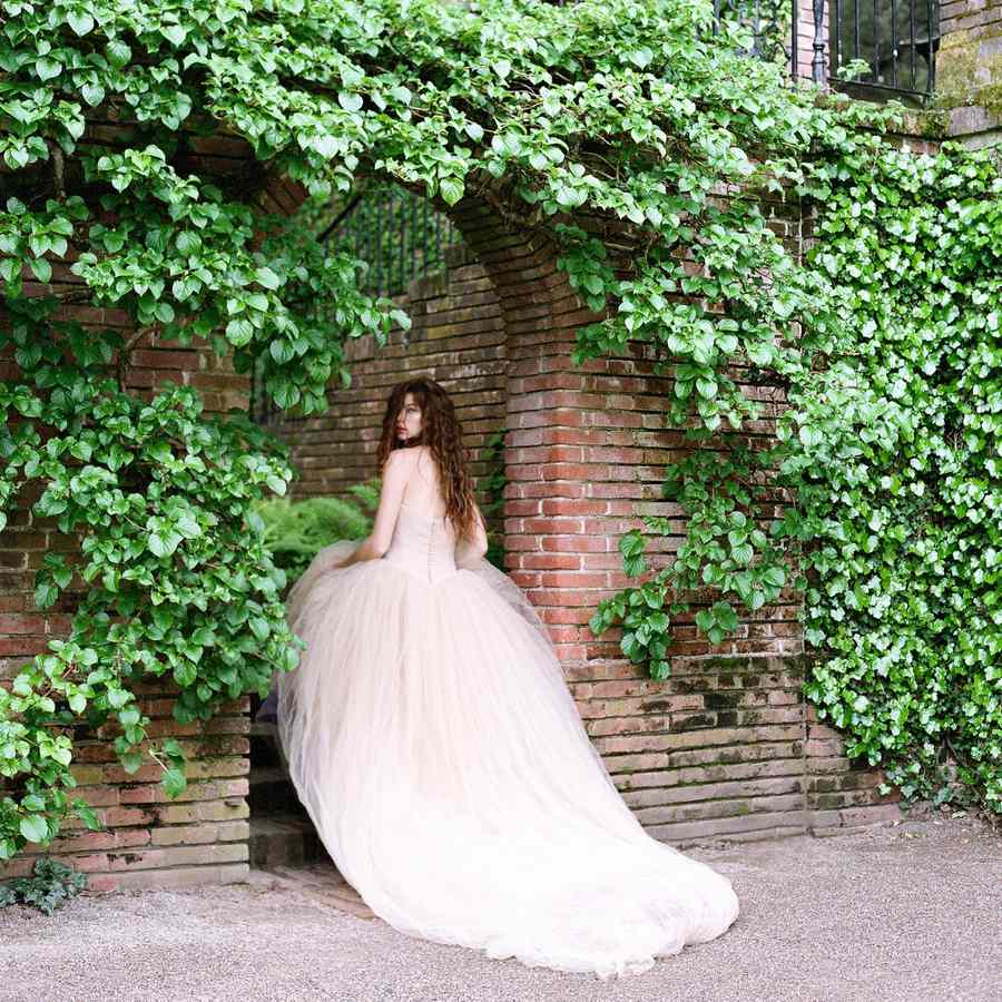 A balletcore bride wearing a tulle wedding dress walking into an ivy-covered venue in California.