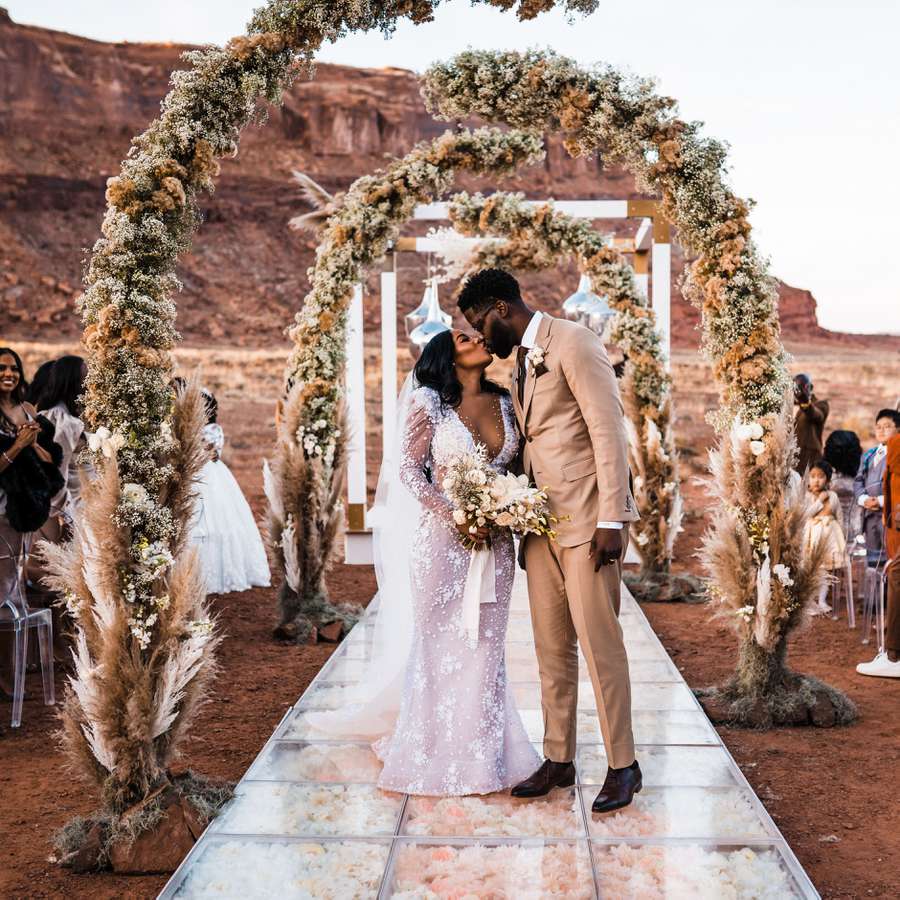 Couple kissing beneath a deconstructed floral arch with pampas grass and dried flowers