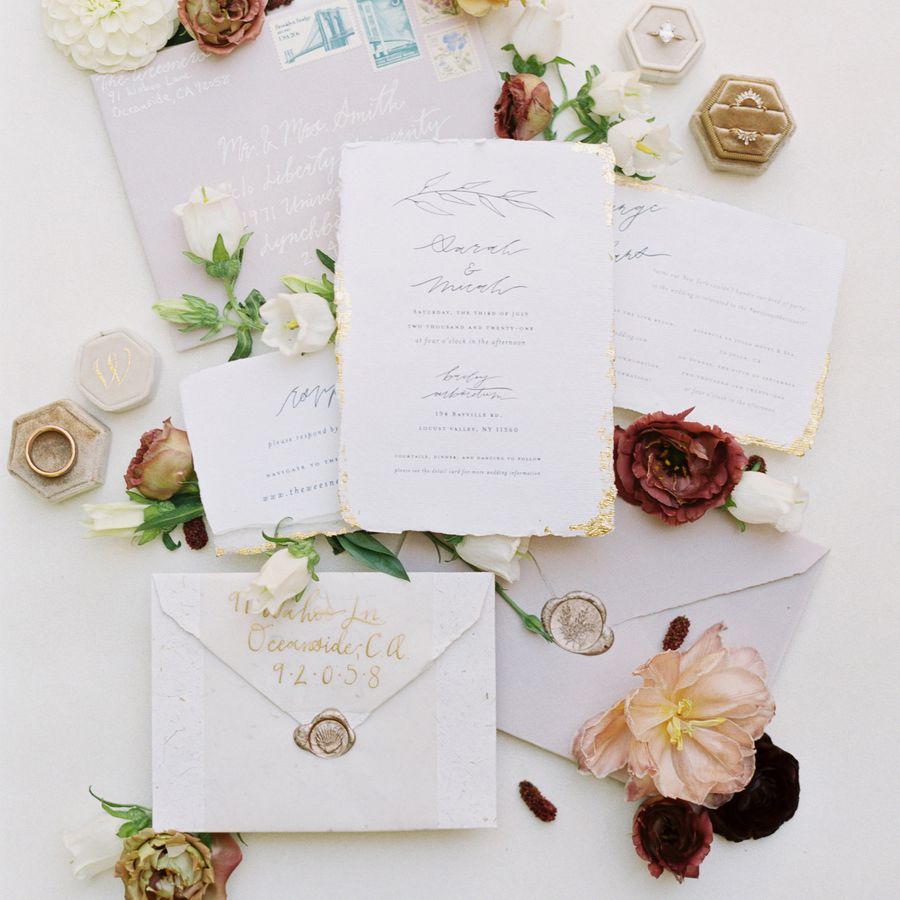 A deckle-edge invitation suite surrounded by colorful flowers.