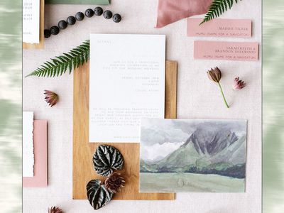 A wedding invitation flat lay with a painting of a mountain on one of the cards