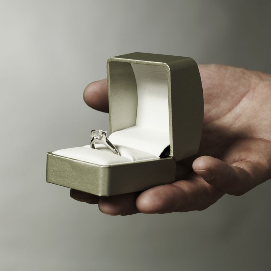 A diamond ring in a light green box that a personâs hand is holding