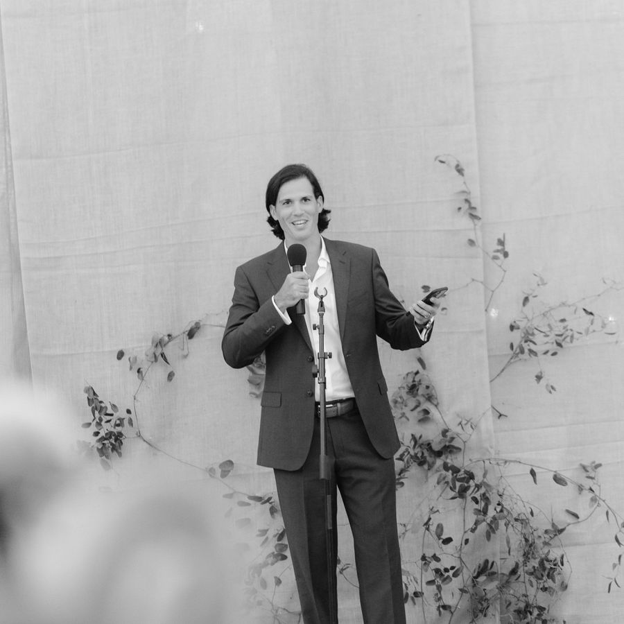 Young Man Giving Rehearsal Dinner Toast at Friend's Wedding with Greenery Backdrop