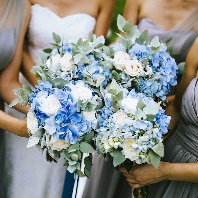 View of bride and bridesmaids holding blue and white flower bouquets during a wedding ceremony.