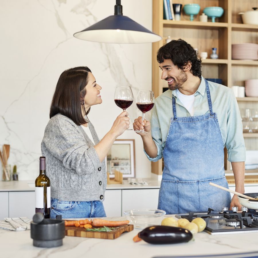 Couple toasting with red wine in their kitchen while making dinner