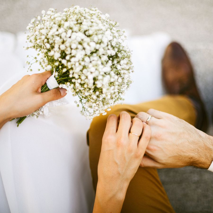 A bride holding a bouquet of baby's breathe holds her groom's hand.