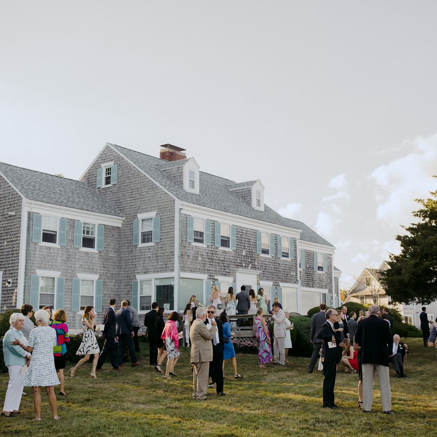 A backyard wedding at a gray and blue house with guests mingling on the lawn.