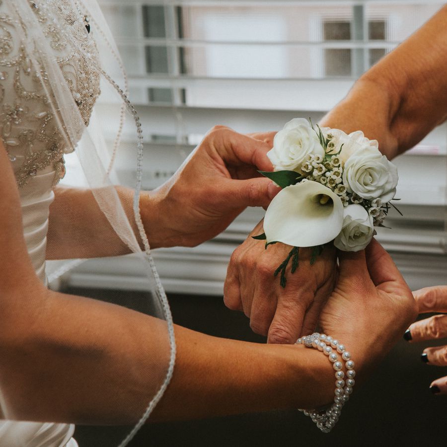 A bride fastening a corsage to the wrist of a wedding party member.
