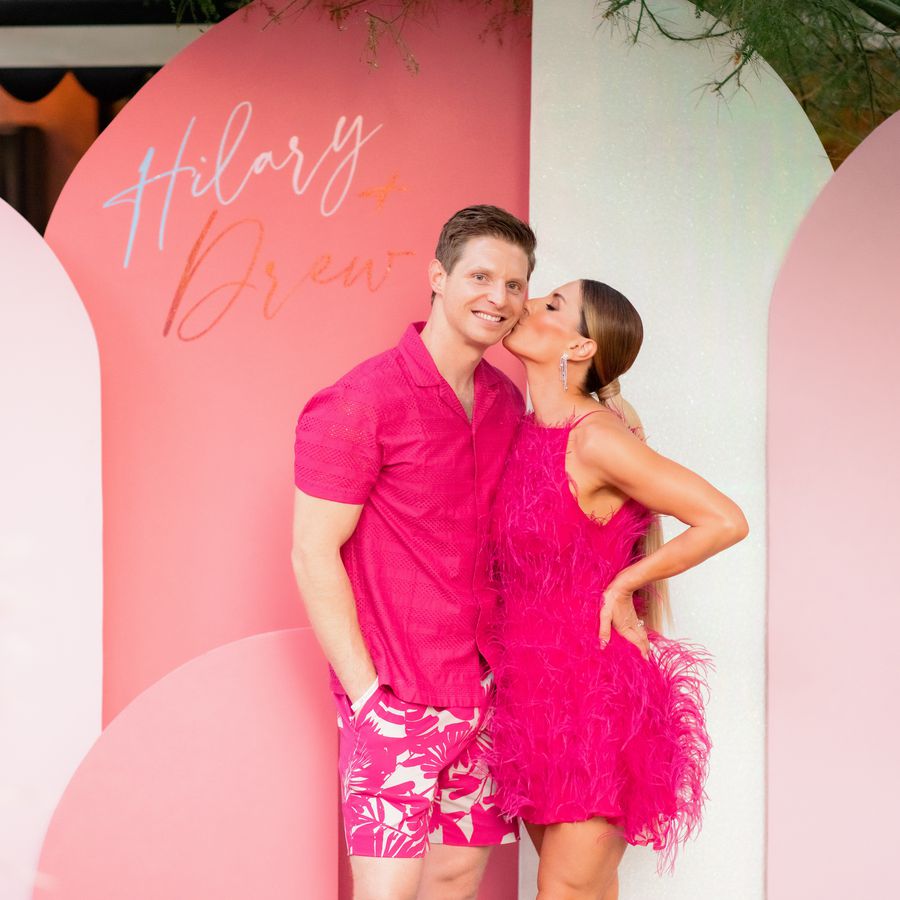 Bride and groom in bright pink outfits in front of a color-blocked sign