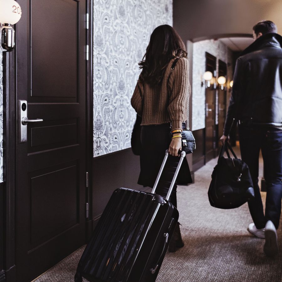 A couple walking with luggage down a hotel hallway.