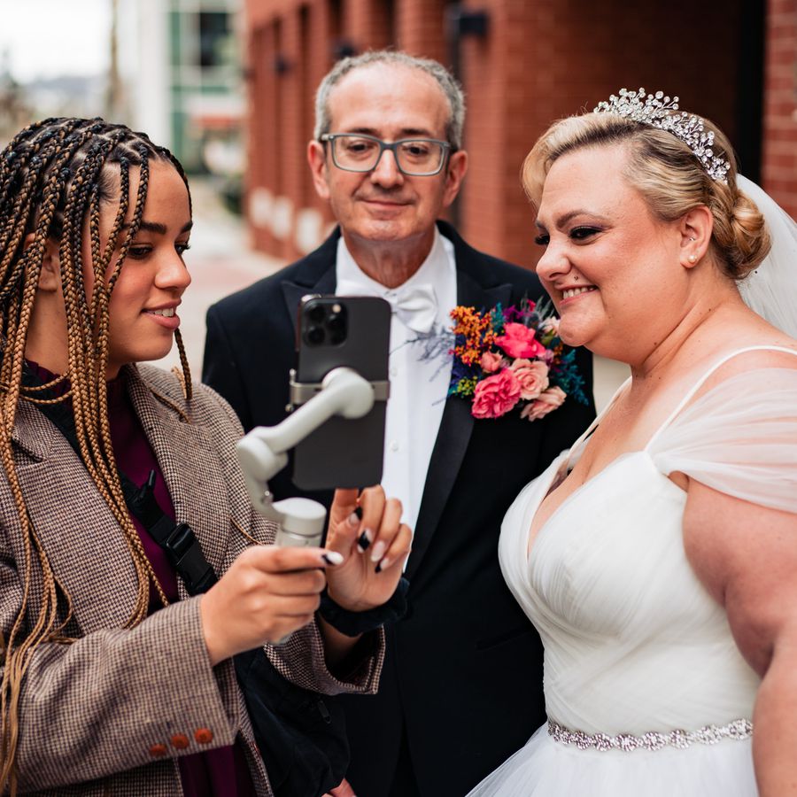 A wedding social content creator looking at an iphone with a bride and groom