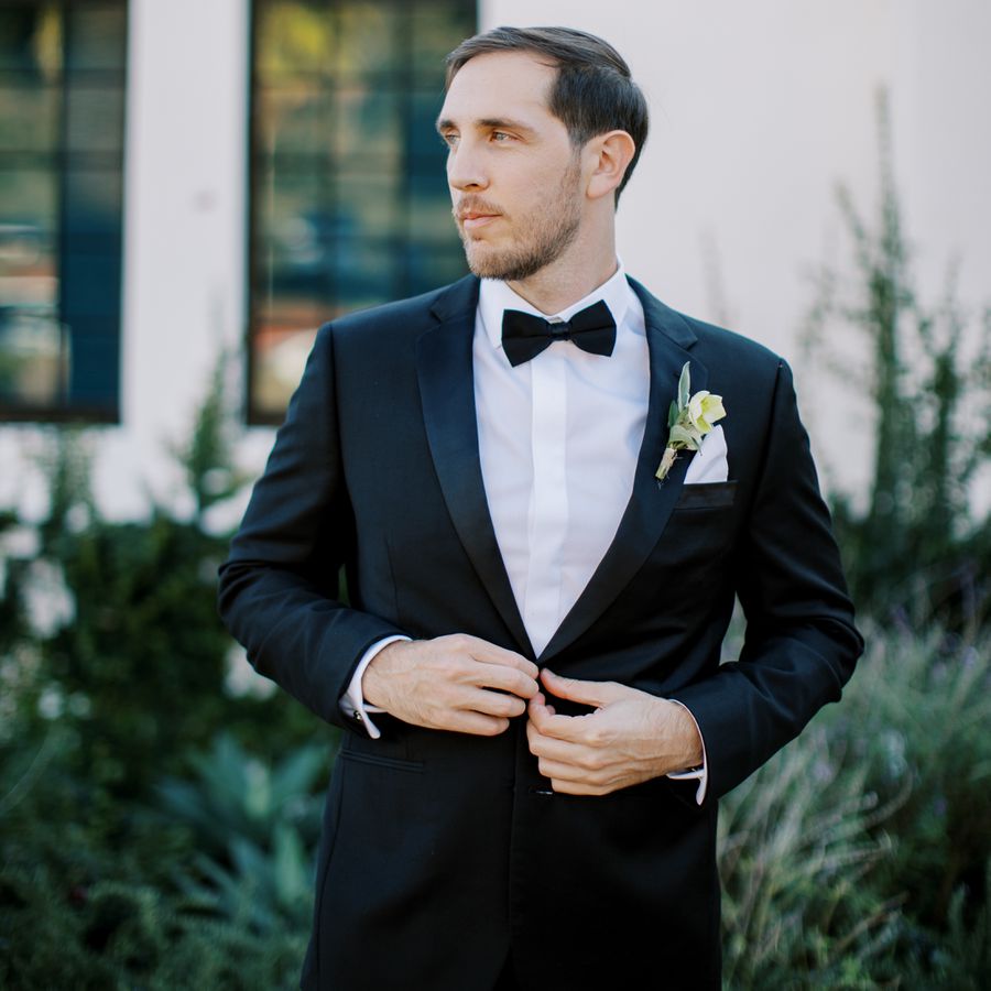 groom looking away wearing a black tuxedo and single flower boutonniÃ¨re
