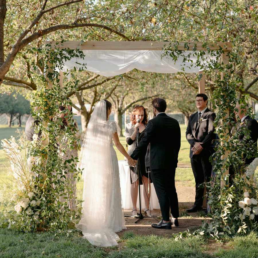 bride and groom under chuppah with greenery