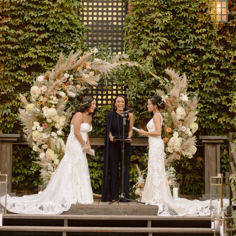 wedding officiant in black gown standing with two brides at wedding ceremony