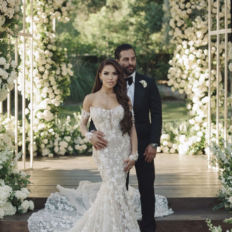 Bride and groom posing in front of a double ceremony arch covered in white roses