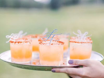 Peach-colored wedding cocktails served in rocks glasses on a silver tray at an outdoor reception.