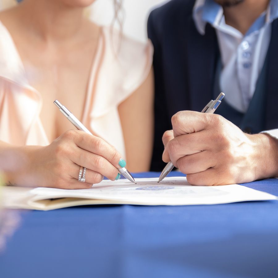 Close-up view of bride and groom signing a marriage certificate, bride wearing a wedding gown and groom dressed in a formal suit.