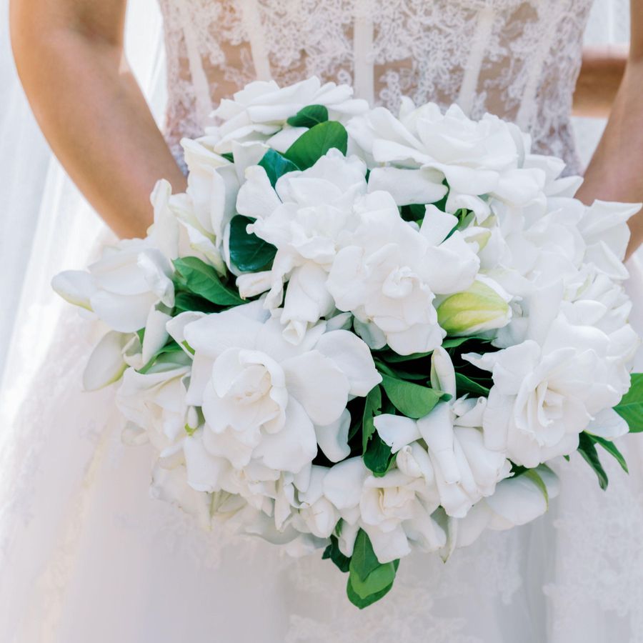 bride in lace bodice holding white gardenia bouquet with green leaves