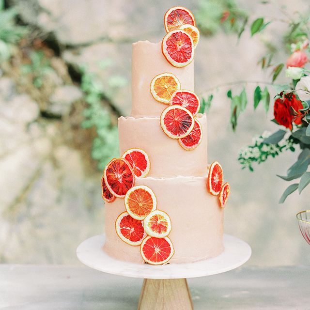 three-tiered wedding cake with blood orange slices against a stone backdrop with greenery