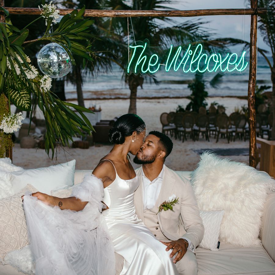 Couple kissing on a monochromatic white couch with a neon sign and disco ball in wedding lounge