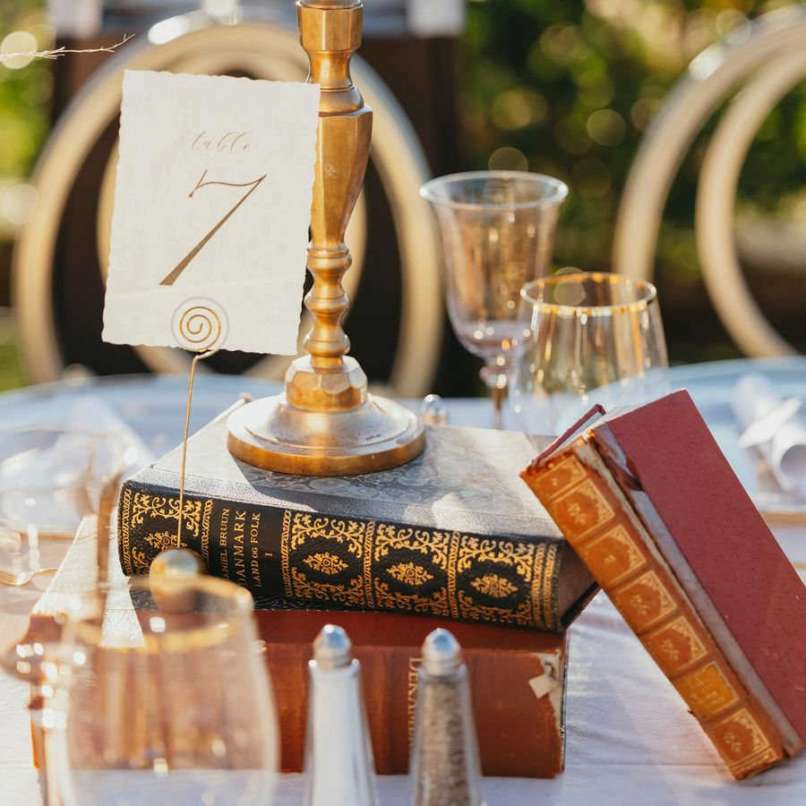 A creative book centerpiece on a wedding reception table with three antique books, a candle, and a table number card.