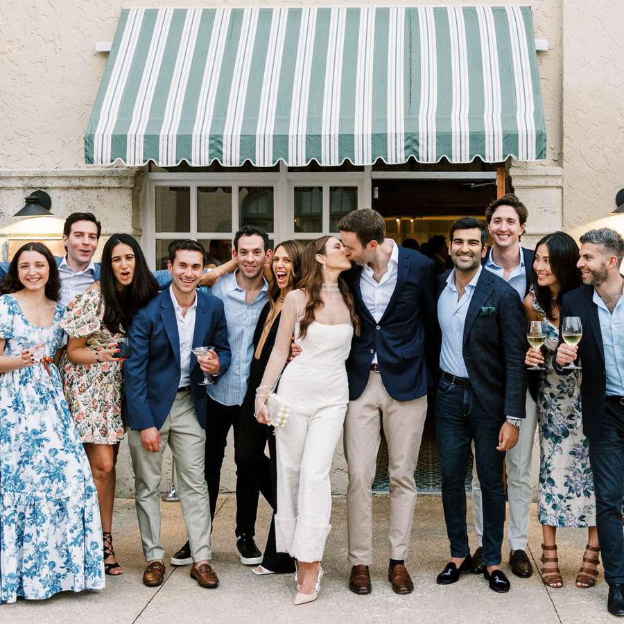 Bride and groom kissing surrounded by millennial wedding guests in patterned dresses and blue suits