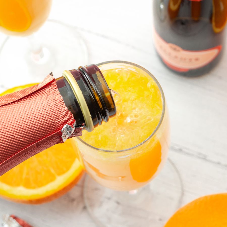 Champagne with a pink label being poured into a champagne flute to make a mimosa with orange juice.