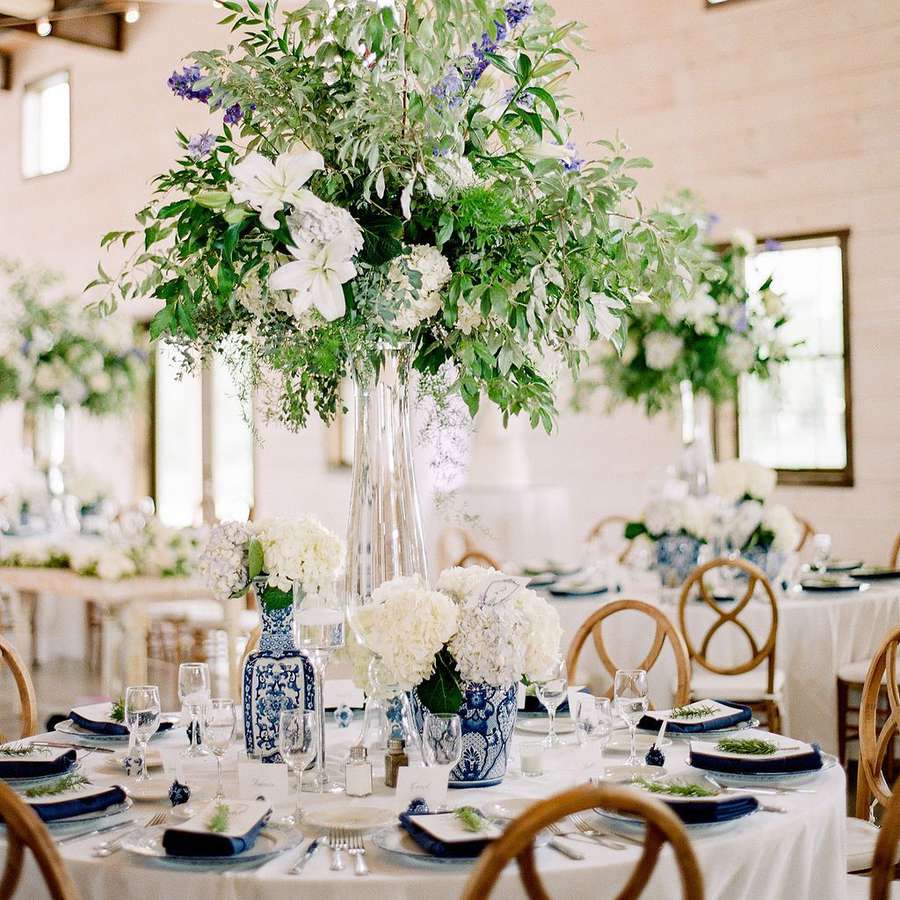 A round table with chinoiserie vases with white flowers, a tall floral centerpiece, navy blue napkins
