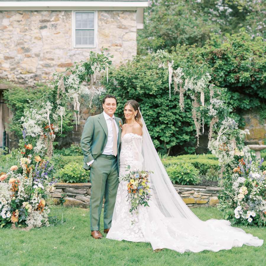 The bride and groom standing in front of their colorful floral arch
