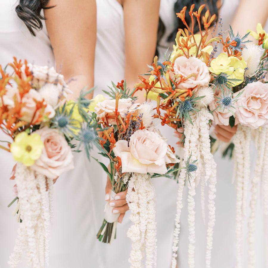 Bridesmaids holding bouquets of amaranthus with pink roses, orange foliage, and yellows blooms