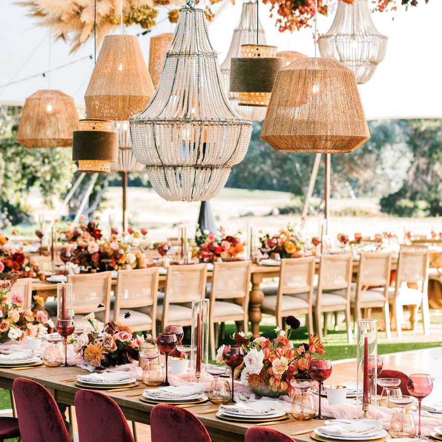 Light fixtures hanging above a wooden table with burgundy taper candles, glassware, flowers, and chairs