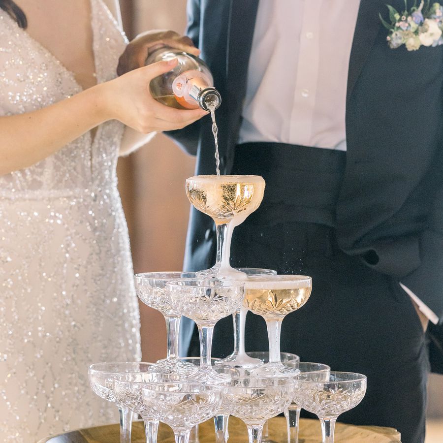 Bride and groom pouring a bottle of pink champagne down a tower of champange coupes at their wedding.