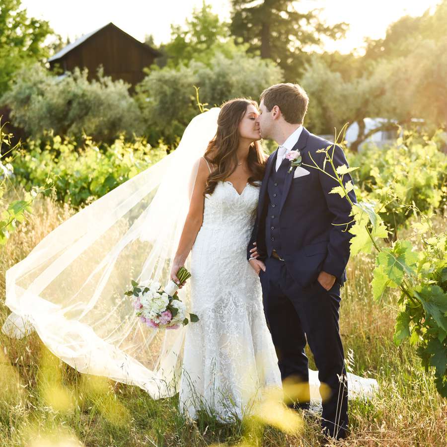 Bride and groom kiss in a green vineyard field at Ru's Farm winery in Sonoma, California