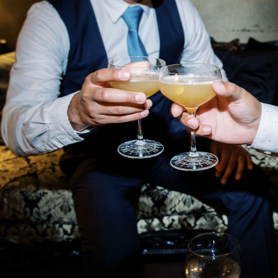 A man in a blue suit, white shirt, and blue tie clinks cocktail glasses with a friend