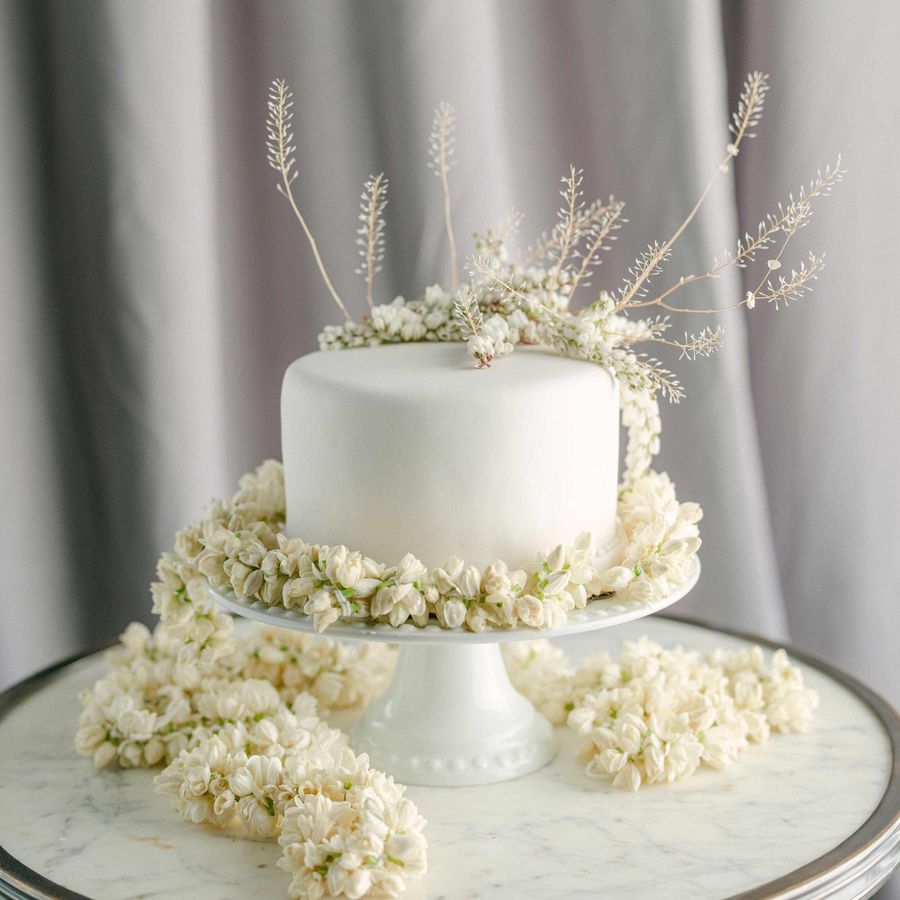 One-tier white wedding cake with dried white rosebuds, florals, and foliage on a cake stand