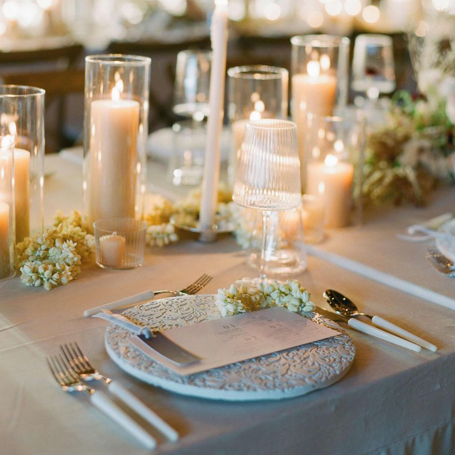 Place settings with white etched chargers, ribbed glassware, white florals, and candles
