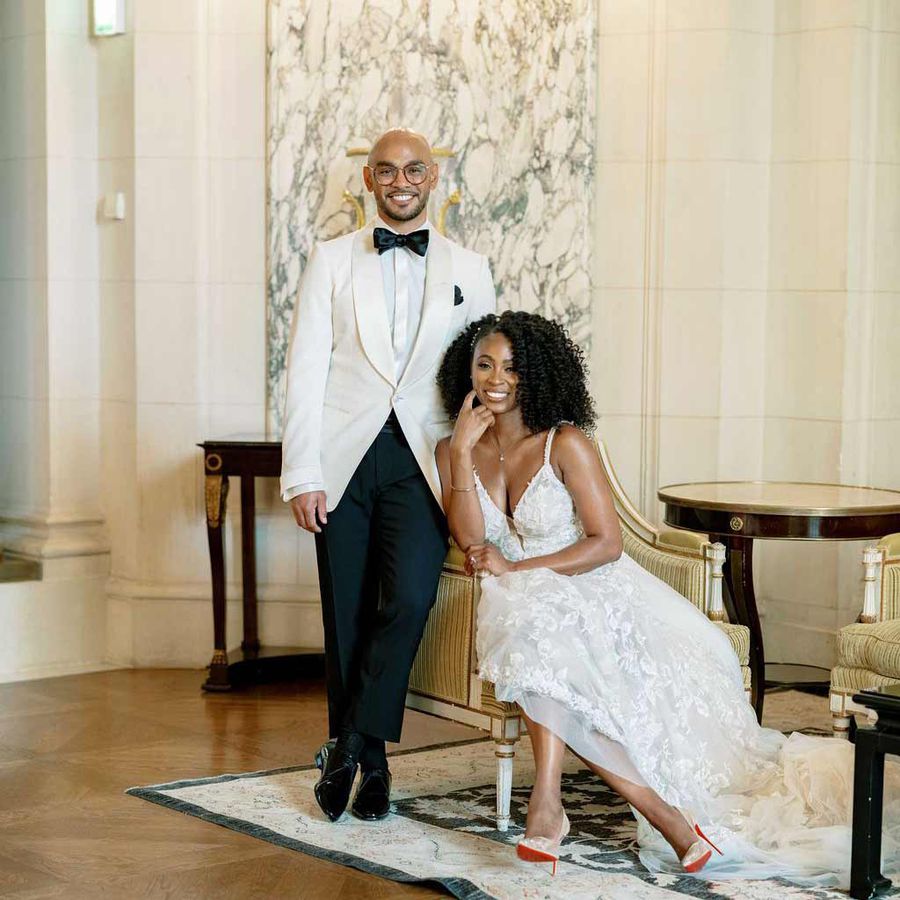 Groom in white tuxedo jacket with black bowtie and pants and sitting bride in white lace gown and red-sole Christian Louboutin pumps