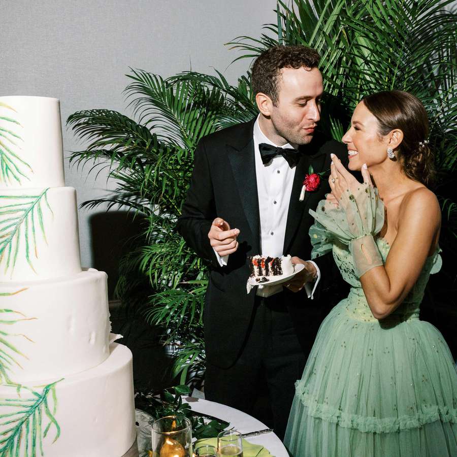 Bride in green dress and groom in tuxedo taste their wedding cake
