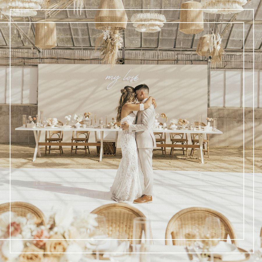A newlywed couple shares a first dance at their wedding reception surrounded by neutral-palette wedding decorations.